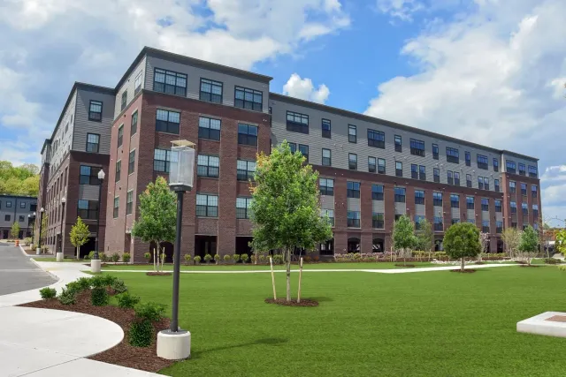 A large brick building with a lot of windows is surrounded by trees and grass.