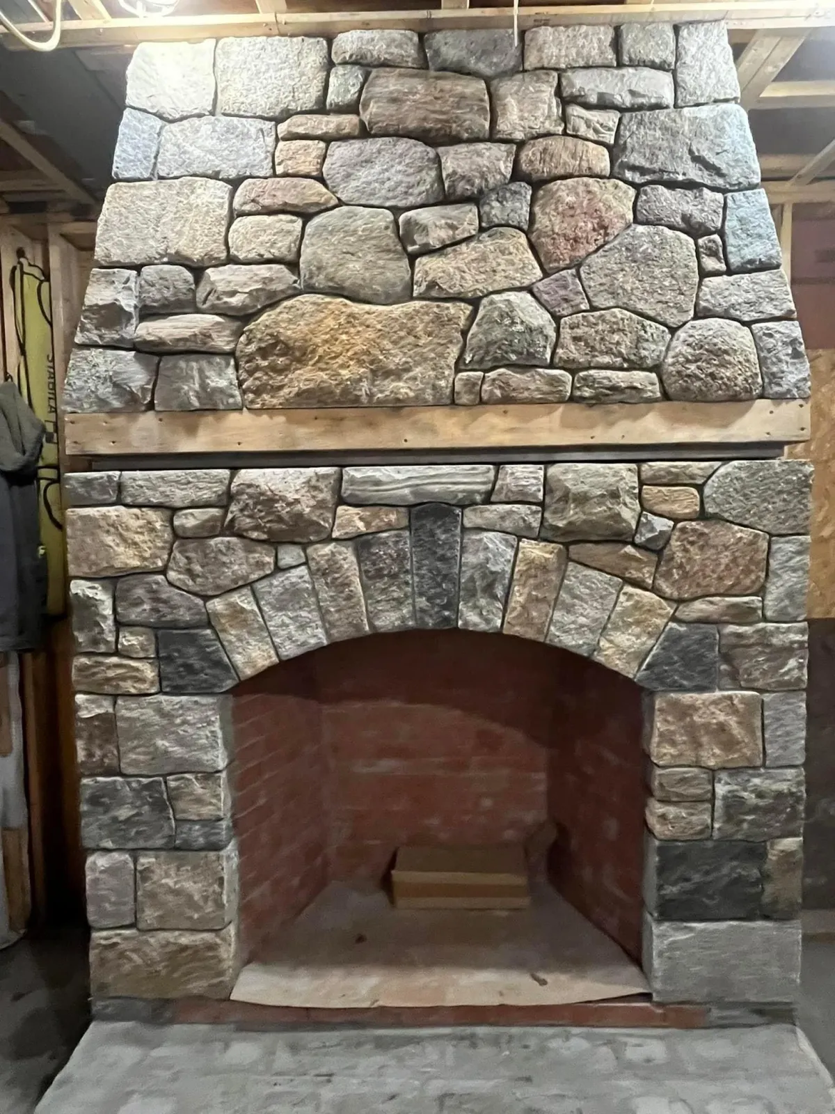 Stone fireplace with arched opening under construction, with wooden framing and brick interior visible.