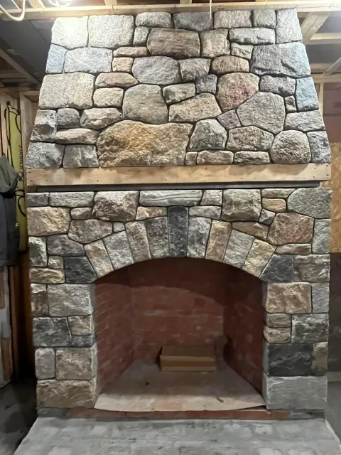 Stone fireplace with arched opening under construction, with wooden framing and brick interior visible.
