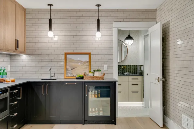 Hardwood floor installation in a Norwell kitchen with a beige brick backsplash, black lower cabinets, pendant lighting, a framed landscape painting, and a view into a bathroom with mirrored black and green tile.