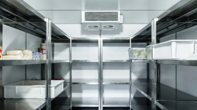 An empty refrigerator with stainless steel shelves in a kitchen.