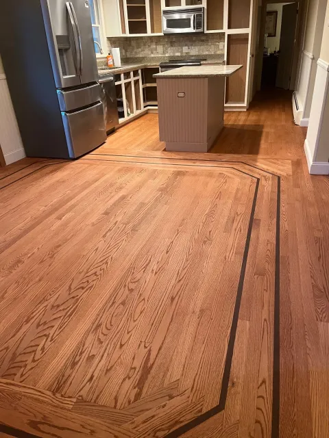 Wooden kitchen floor with a dark border, stainless steel appliances, and a central island.