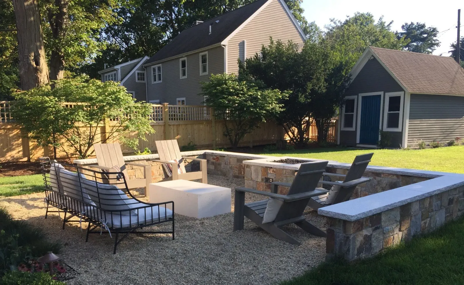 A backyard with a fire pit and chairs in front of a house.