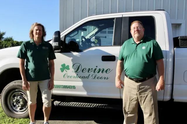 Two people in green shirts stand by a white truck with