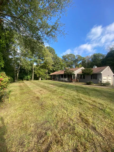A house is sitting on top of a lush green field surrounded by trees.