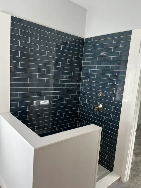 Navy subway tile walls and shower valve seen over the half wall