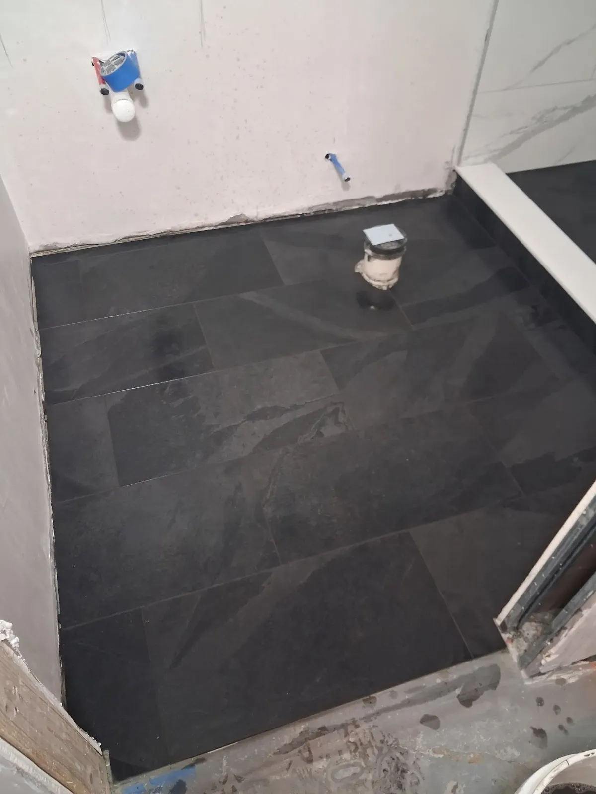 Small tiled bathroom floor under renovation with a toilet flange and exposed plumbing fittings.