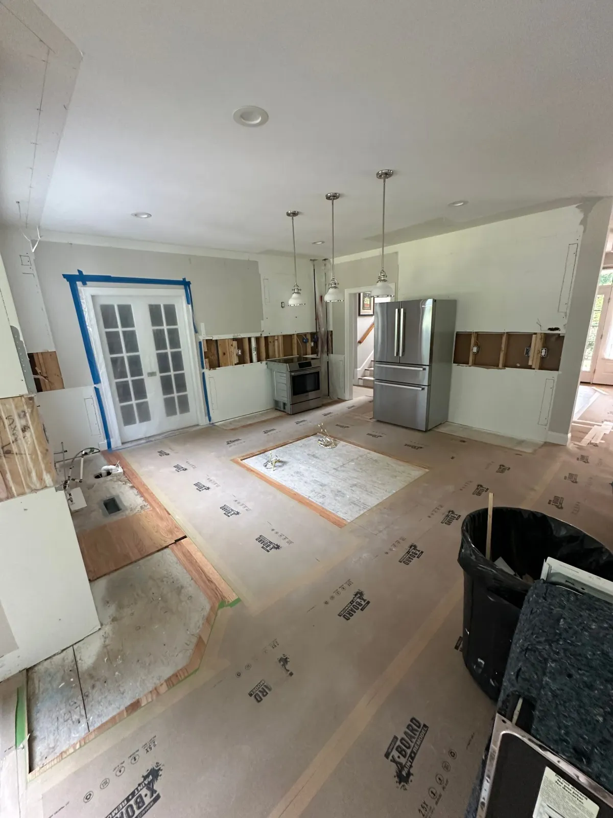 A kitchen under construction with a stainless steel refrigerator.