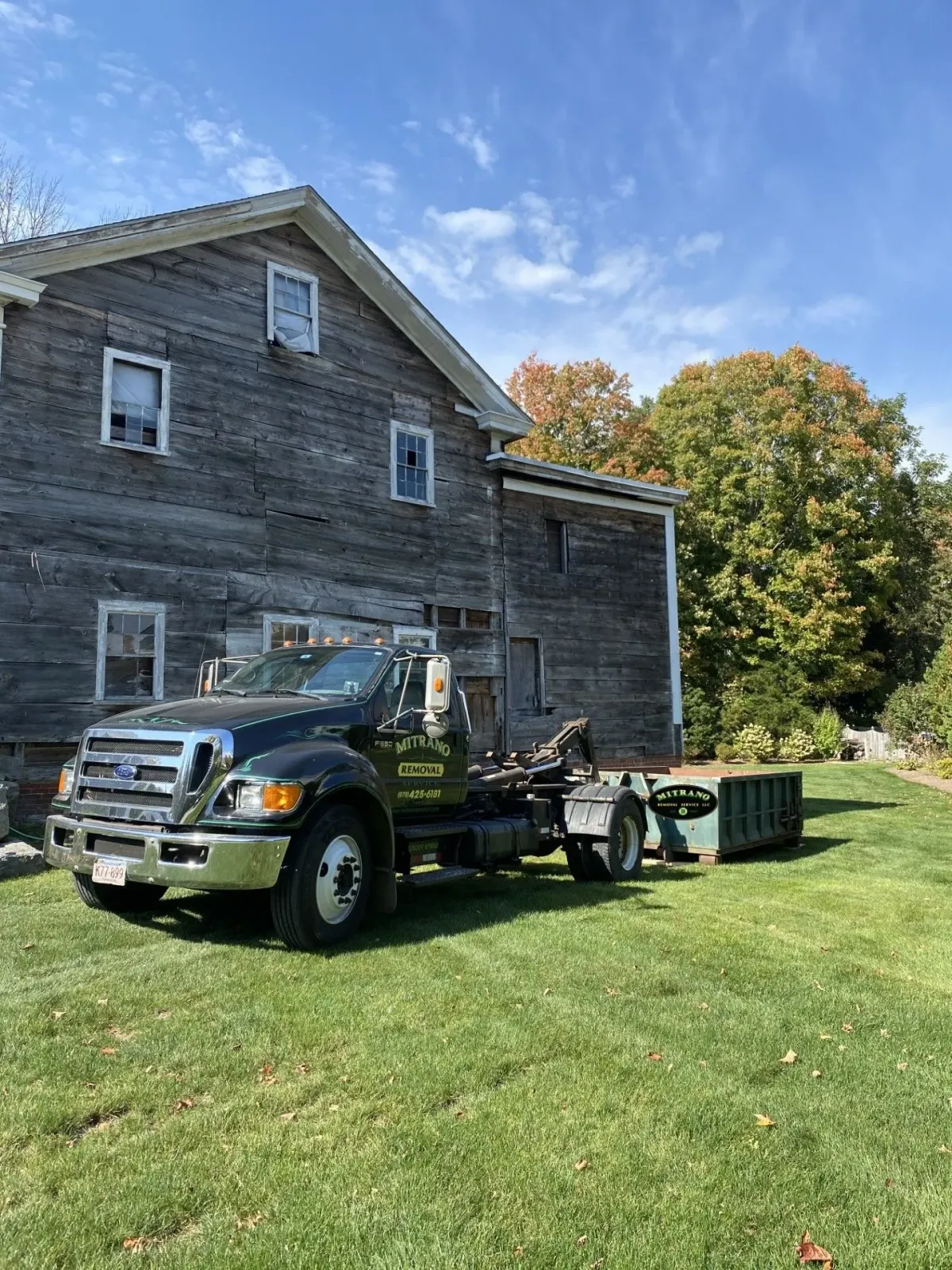 Black dump truck next to weathered wooden house, green lawn, sunny day.