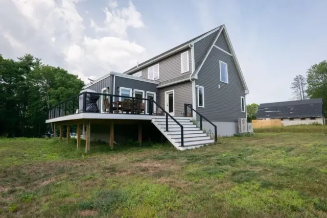Modern home exterior with gray siding, large deck featuring black railing, and steps leading to the yard, showcasing a custom residential build in a natural setting.