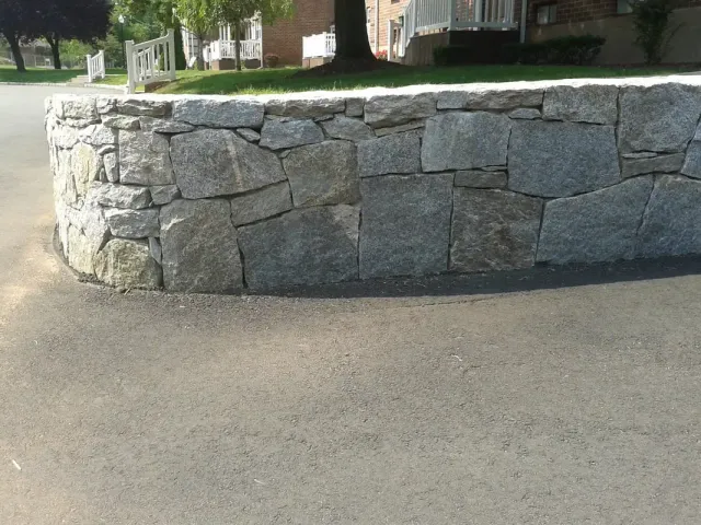 Curved natural stone retaining wall holding a grade along a driveway