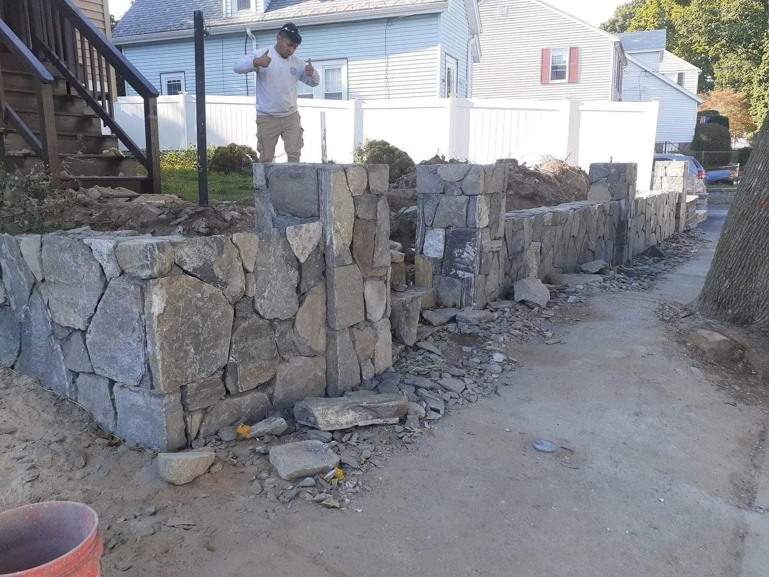 Stone retaining wall beside a dirt path, with a person standing near white houses in the background