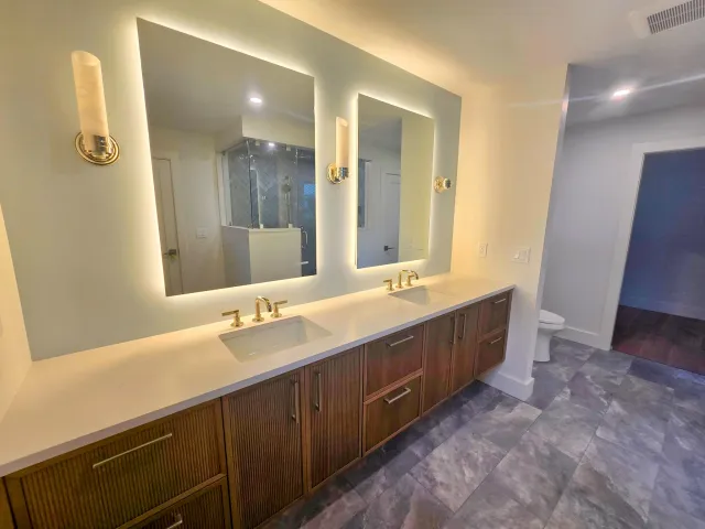 Rectangular backlit mirrors and wall sconces above a long wood double vanity.