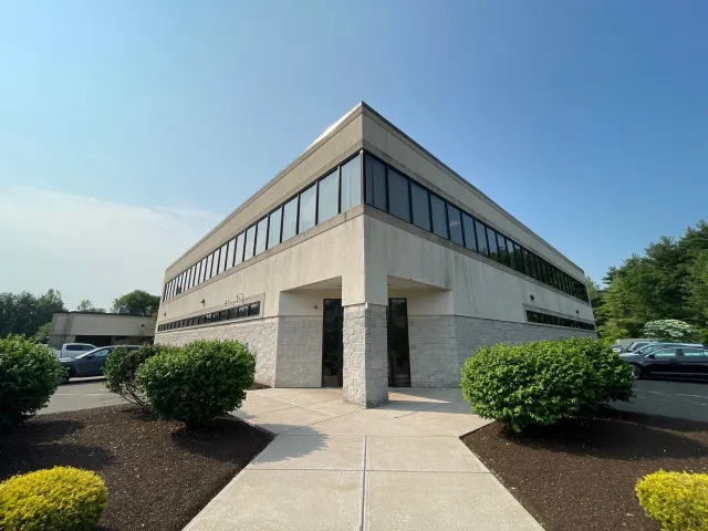 A large building with a lot of windows is surrounded by bushes and trees.
