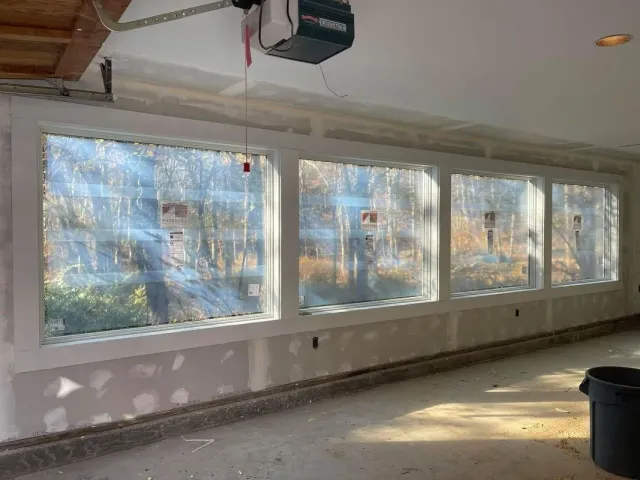 Three large rectangular windows in a room under construction, with visible forest outside.