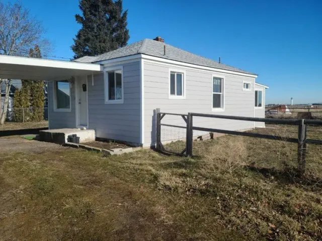 New white siding on a house with a carport, fenced yard, and a clear blue sky.