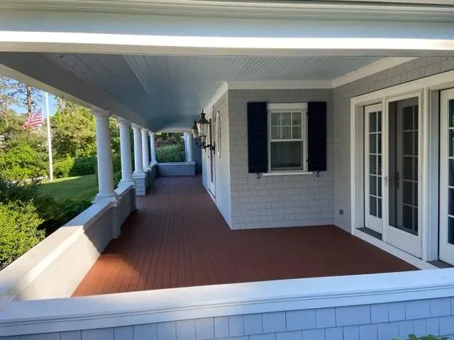 Covered front porch with white columns, red floor, and white brick walls beside a lawn.