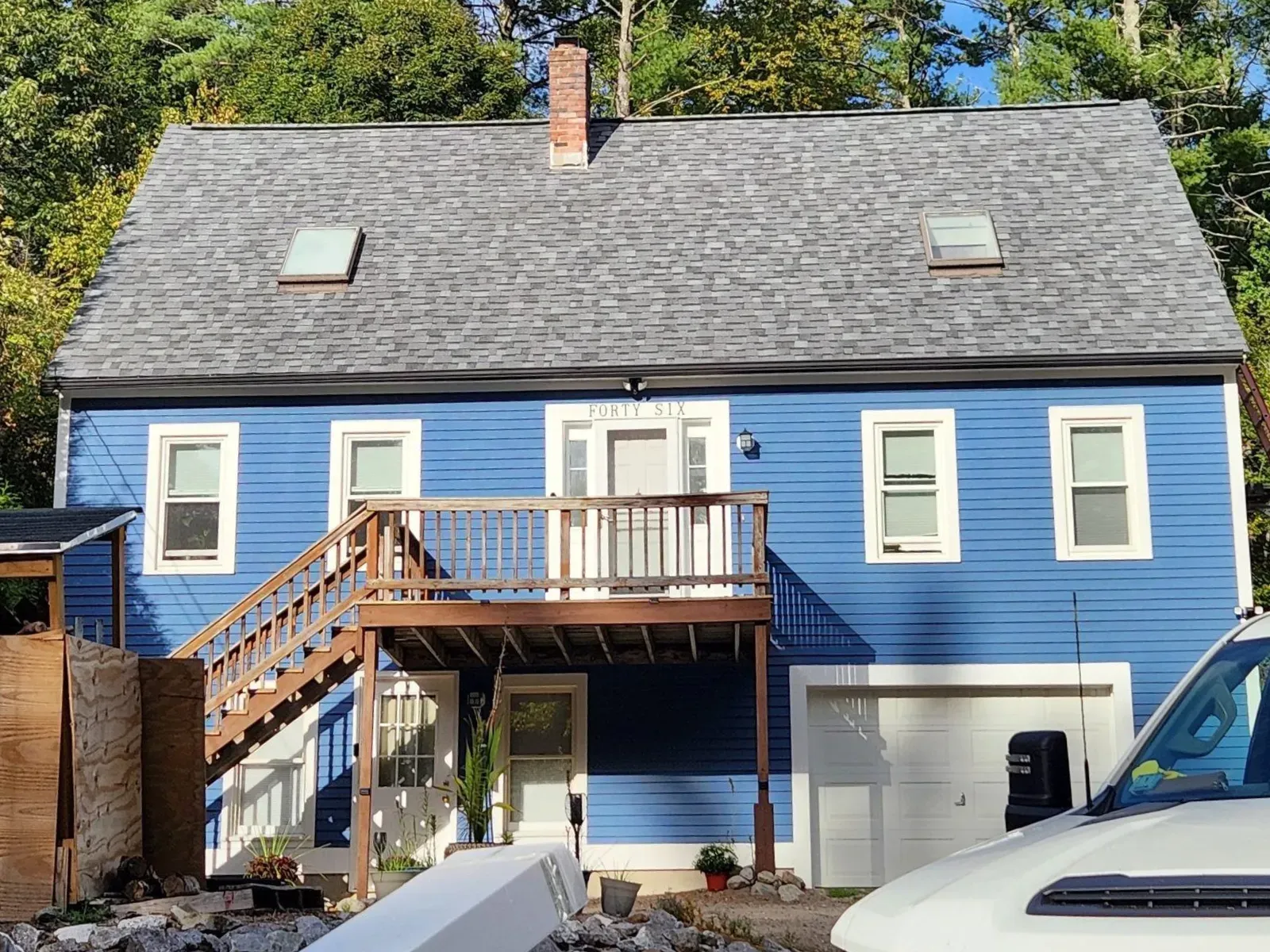 Blue house with gray roof, deck, and garage door. Wooden stairs lead to the deck.