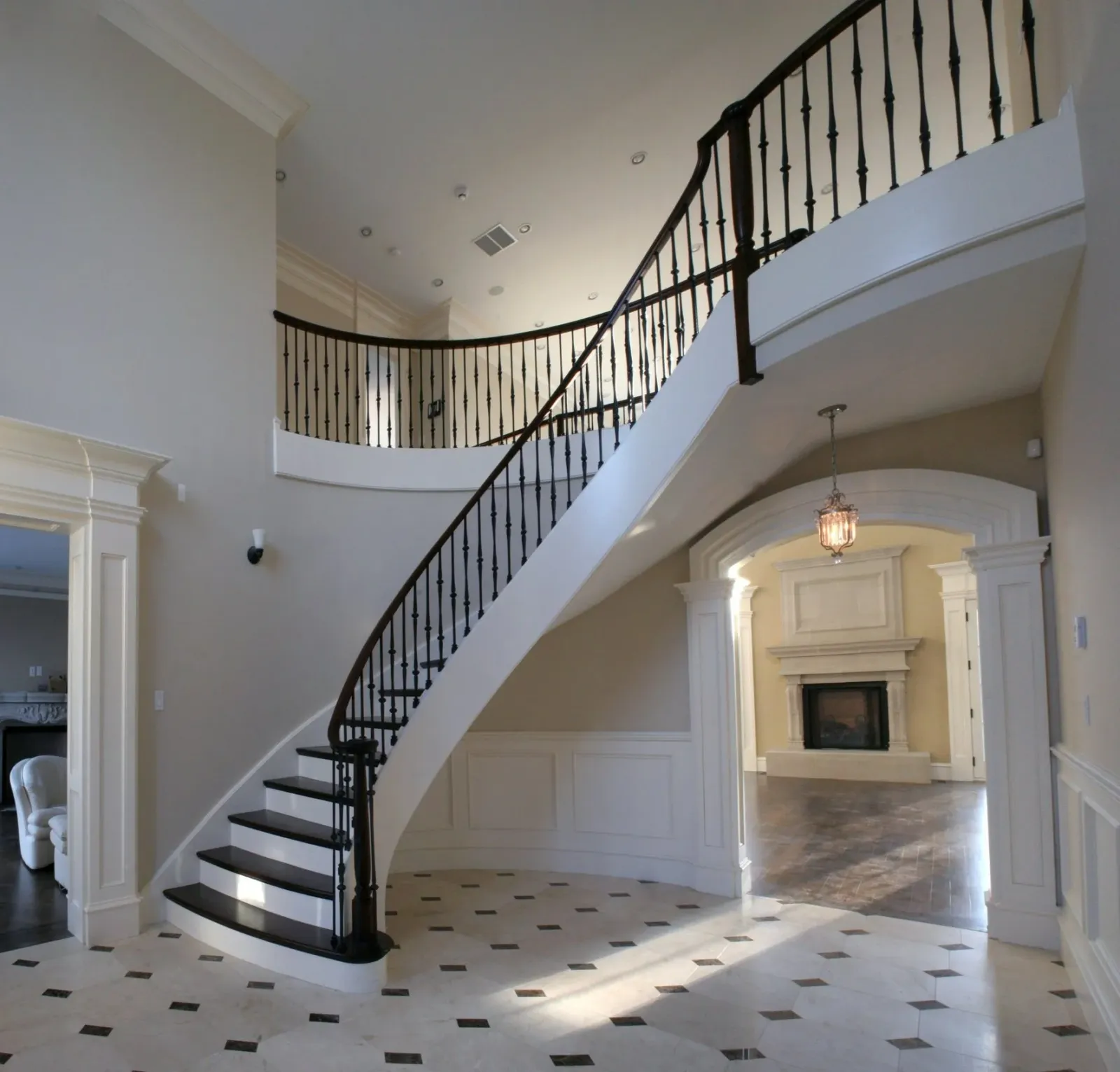 Elegant foyer with spiral staircase, marble flooring, and a fireplace with detailed mantel in the background.
