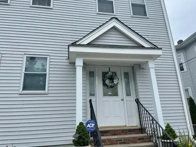 Gray multi-story house with white front door, porch, and security sign.
