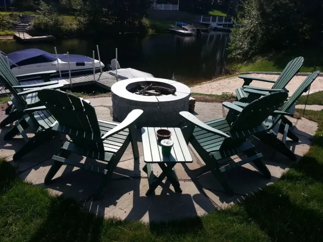 Green Adirondack chairs gathered around a stone fire pit near the lake