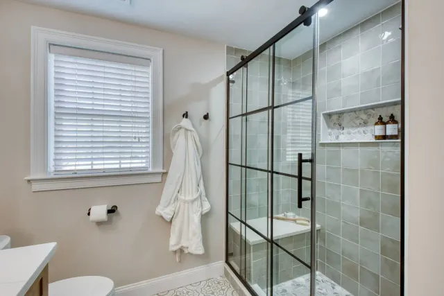 Modern bathroom with glass shower, tiled walls, window, and hanging white robe