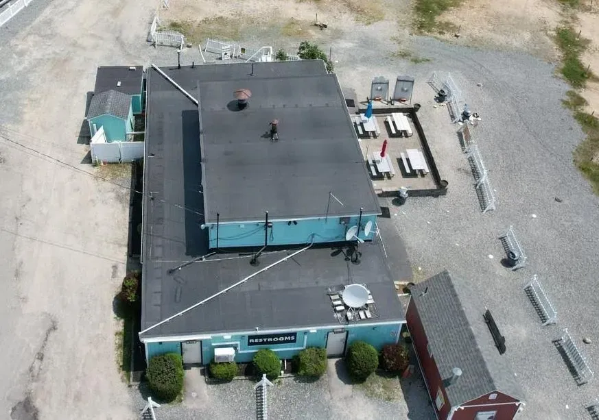 Aerial view of a flat-roofed teal building with nearby parking and gravel lot.
