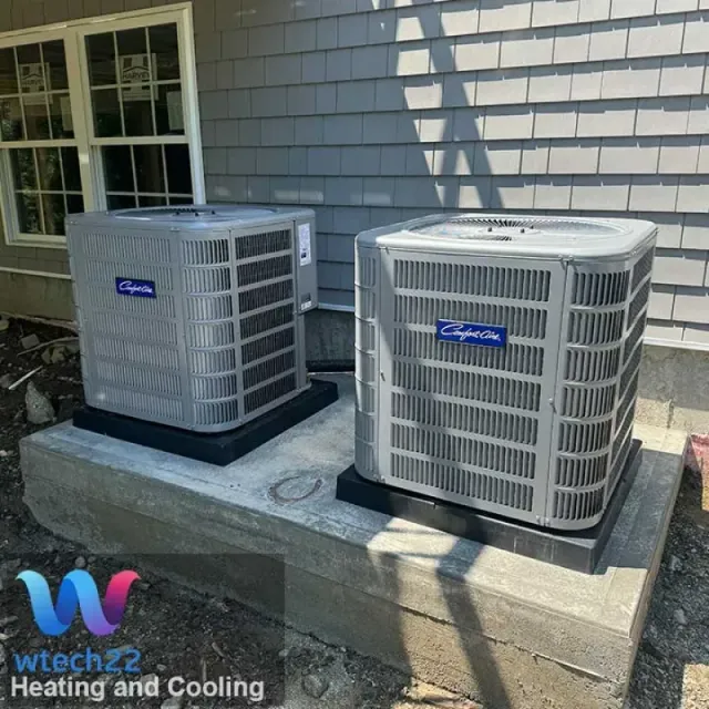 Two gray air conditioning units on concrete slab next to a building with gray siding.
