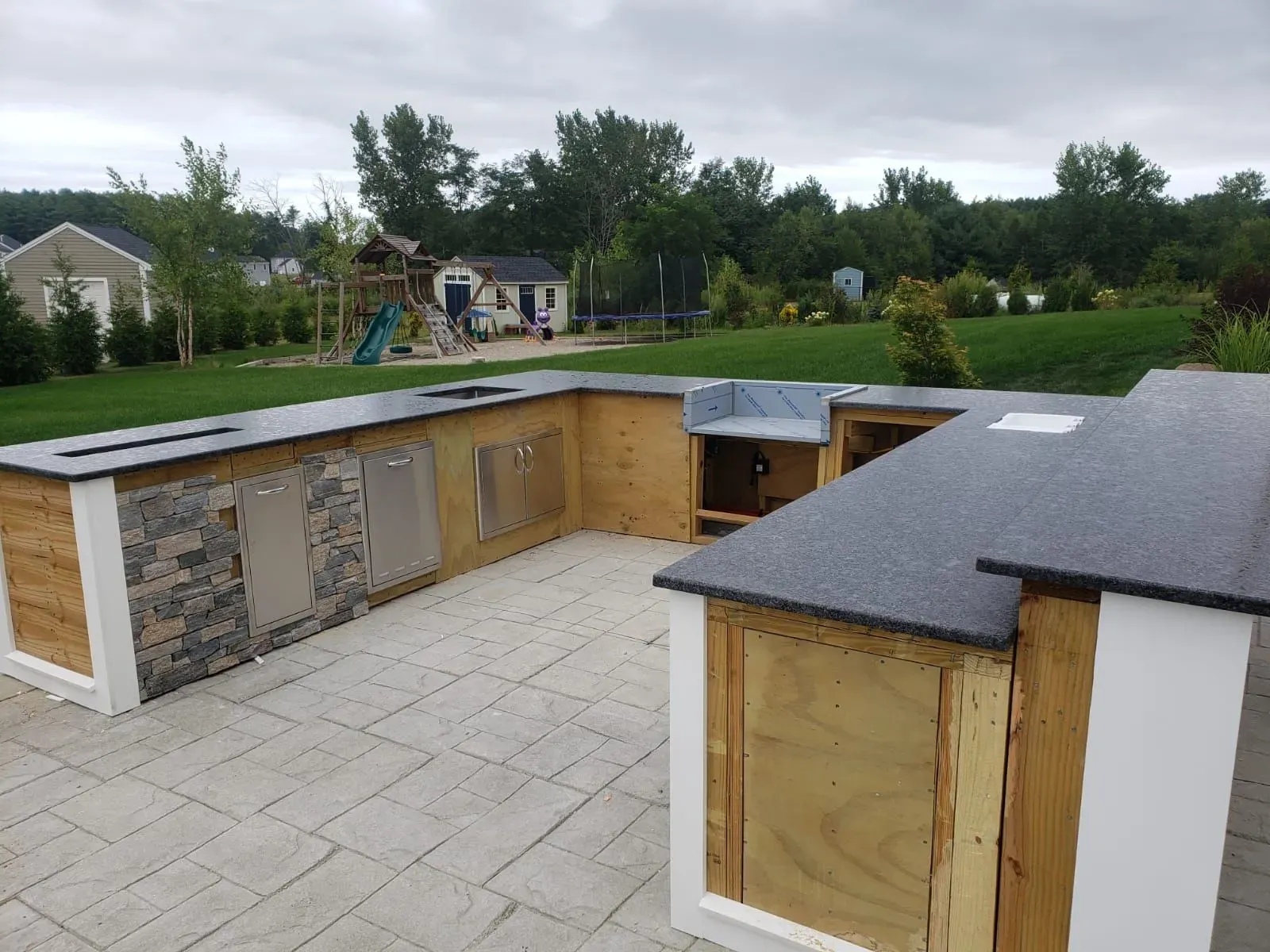 Outdoor kitchen under construction with a granite countertop and wood cabinets.