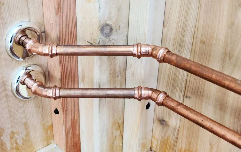 Two copper pipes connected to wall-mounted fixtures against a wooden wall.