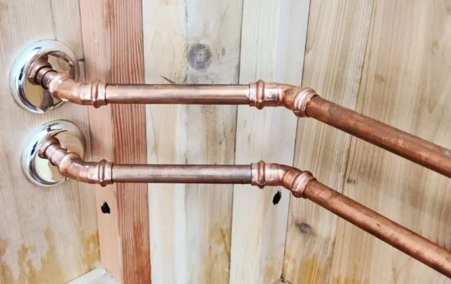 Two copper pipes connected to wall-mounted fixtures against a wooden wall.