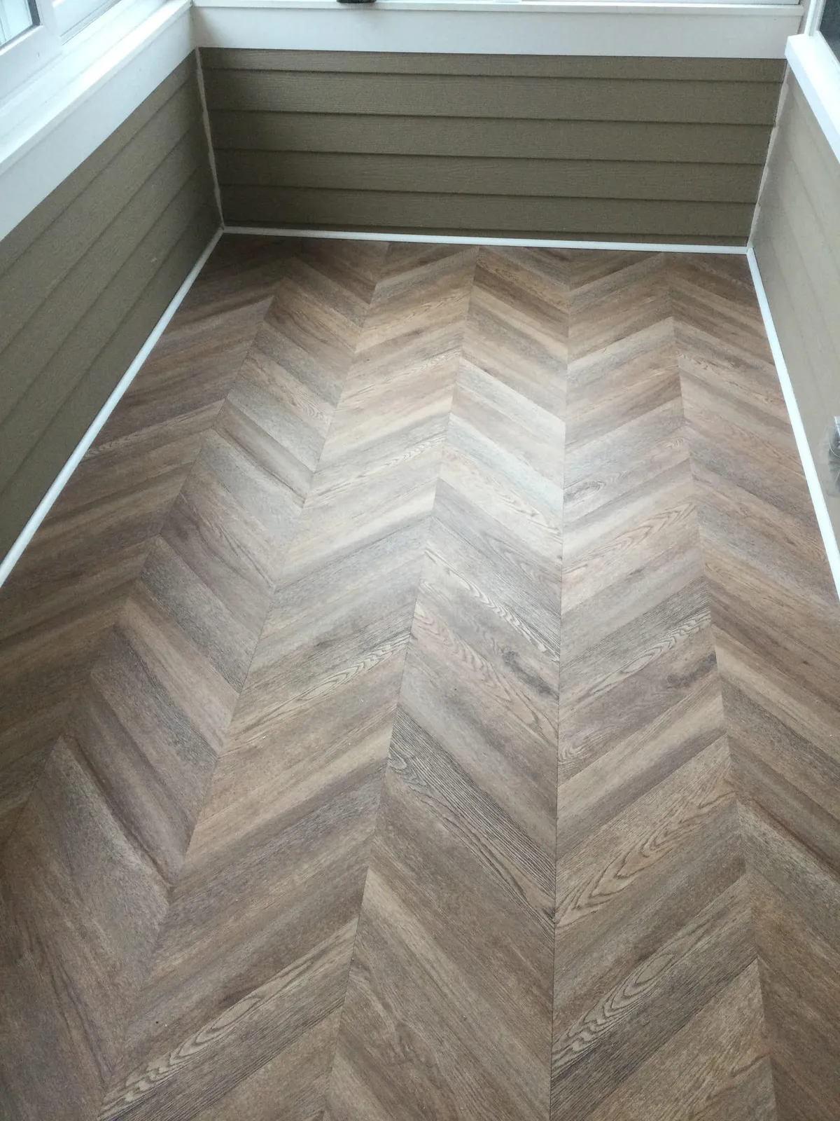 Chevron-pattern luxury vinyl plank floor installed in a sunroom