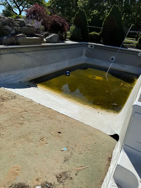 Drained pool with the old liner coming out and murky water in the deep end