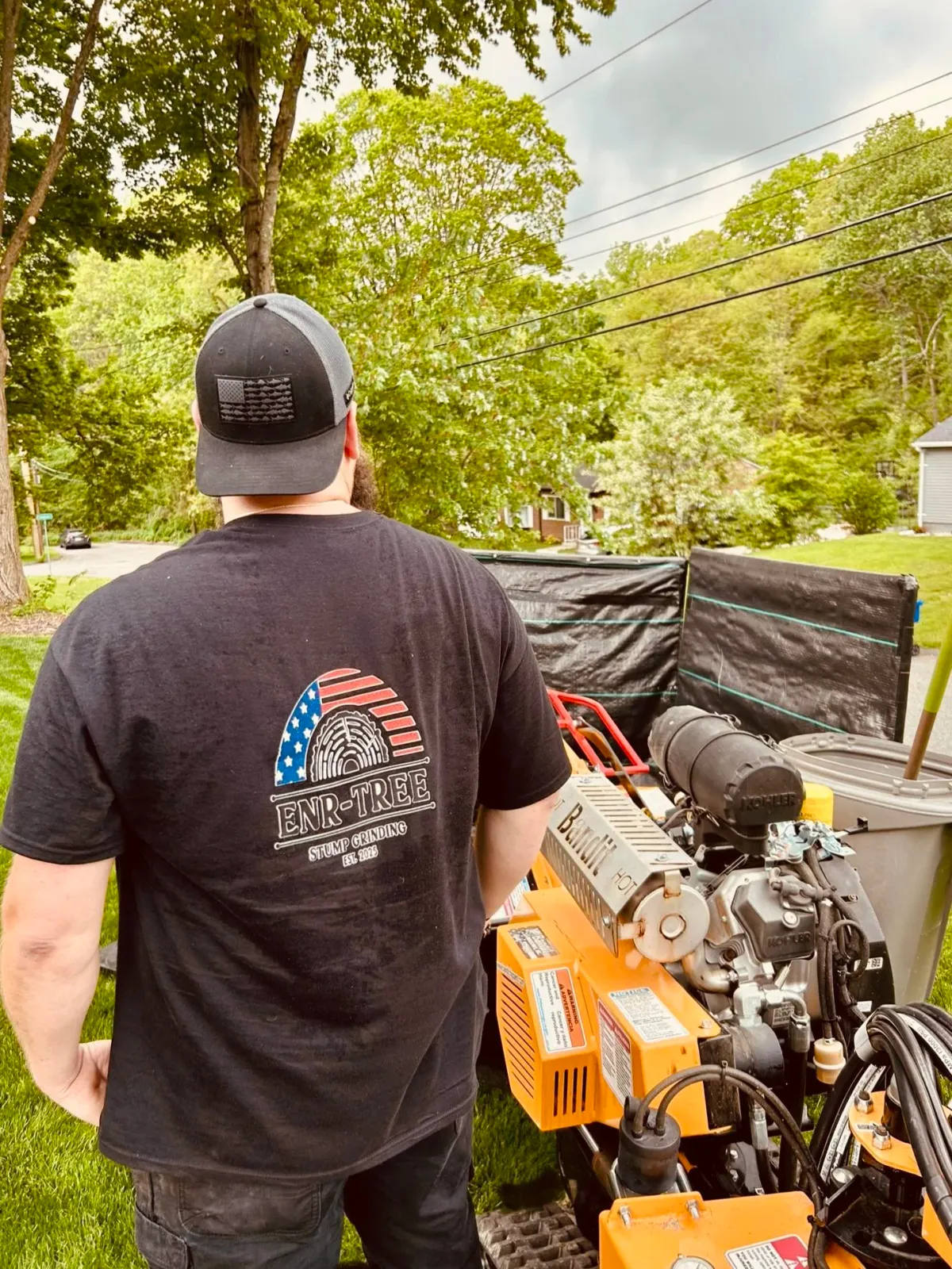 Man standing outdoors next to a piece of equipment with an American flag and a fingerprint logo on his black T-shirt.