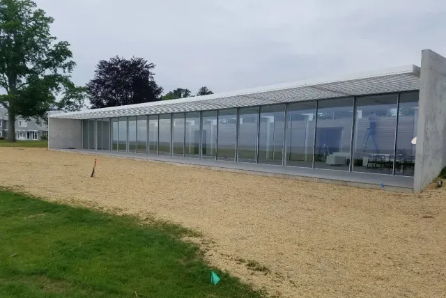 Low glass pavilion with corrugated roof beside a gravel path and grassy lawn