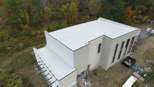 Aerial view of a white modern building with a flat roof in a wooded area.