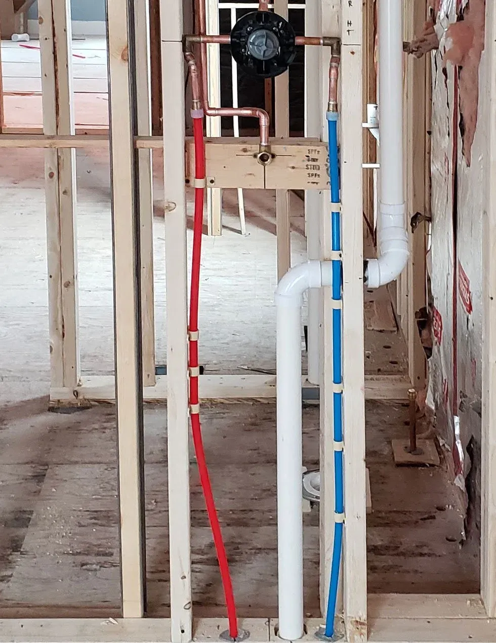 Plumbing pipes including red and blue water supply lines in a framed construction wall.