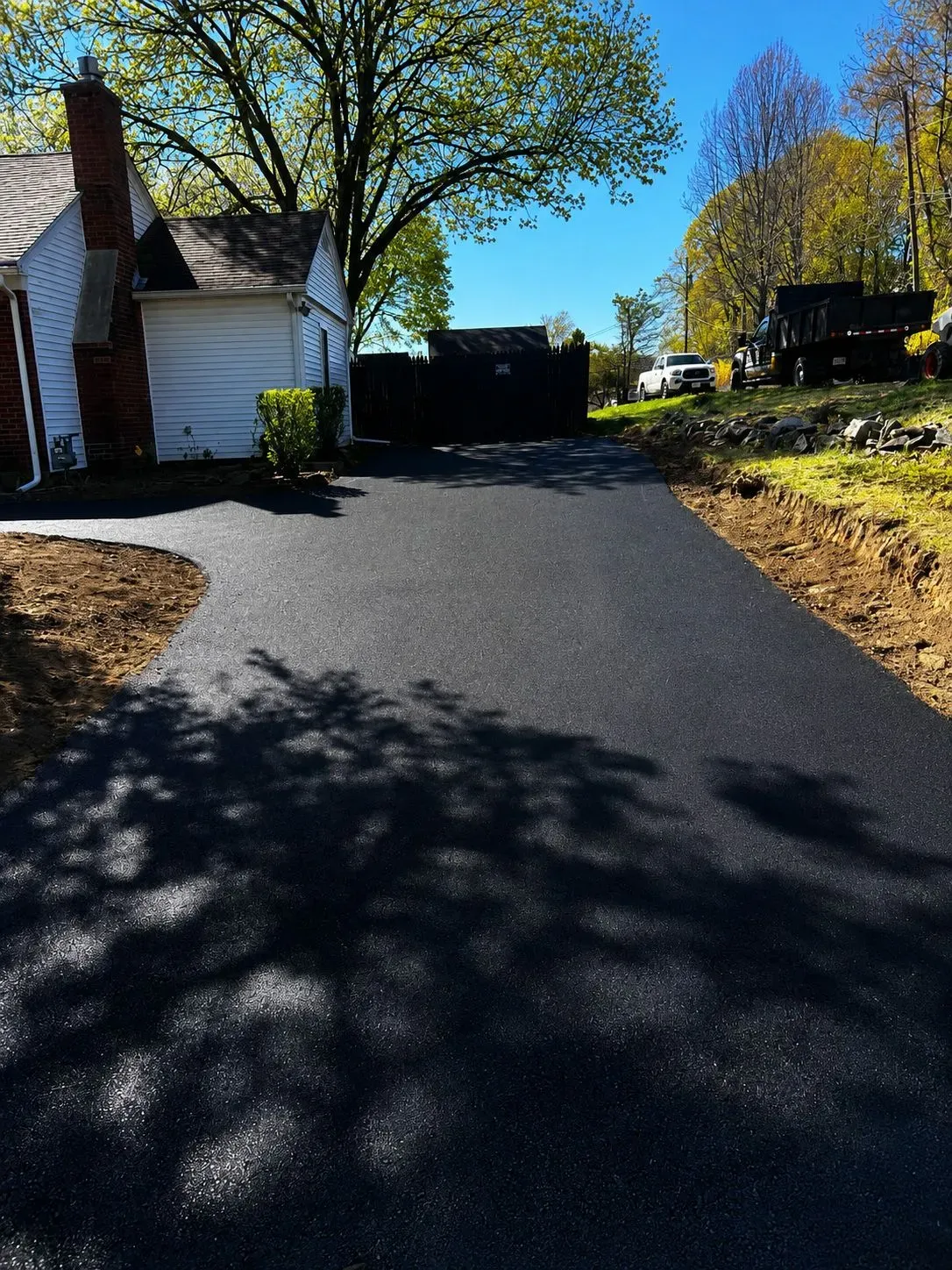 Driveway beside a white house and trees on a sunny autumn day, with long shadows on the pavement