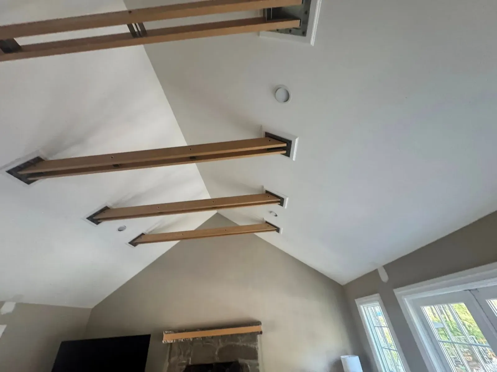 Vaulted ceiling with exposed wooden beams and skylights above a room with a fireplace.