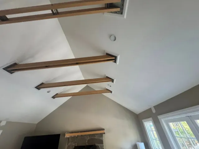 Vaulted ceiling with exposed wooden beams and skylights above a room with a fireplace.