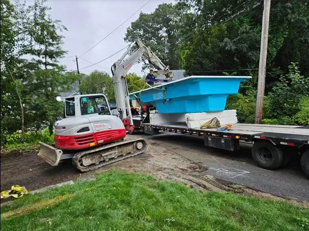 A bulldozer is carrying a large blue pool on a trailer.