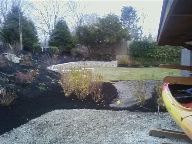 Backyard garden with gravel path, lawn, shrubs, and a yellow kayak at the right edge