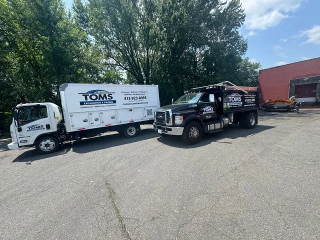 Two service trucks, one white and one black, parked outside. Trees in background.