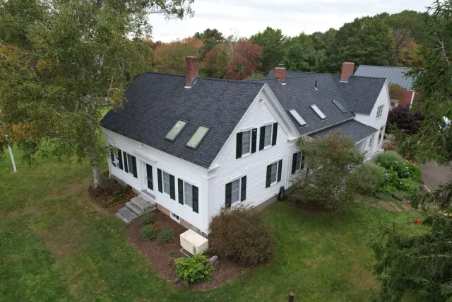 White house with dark roof, black shutters, and trees