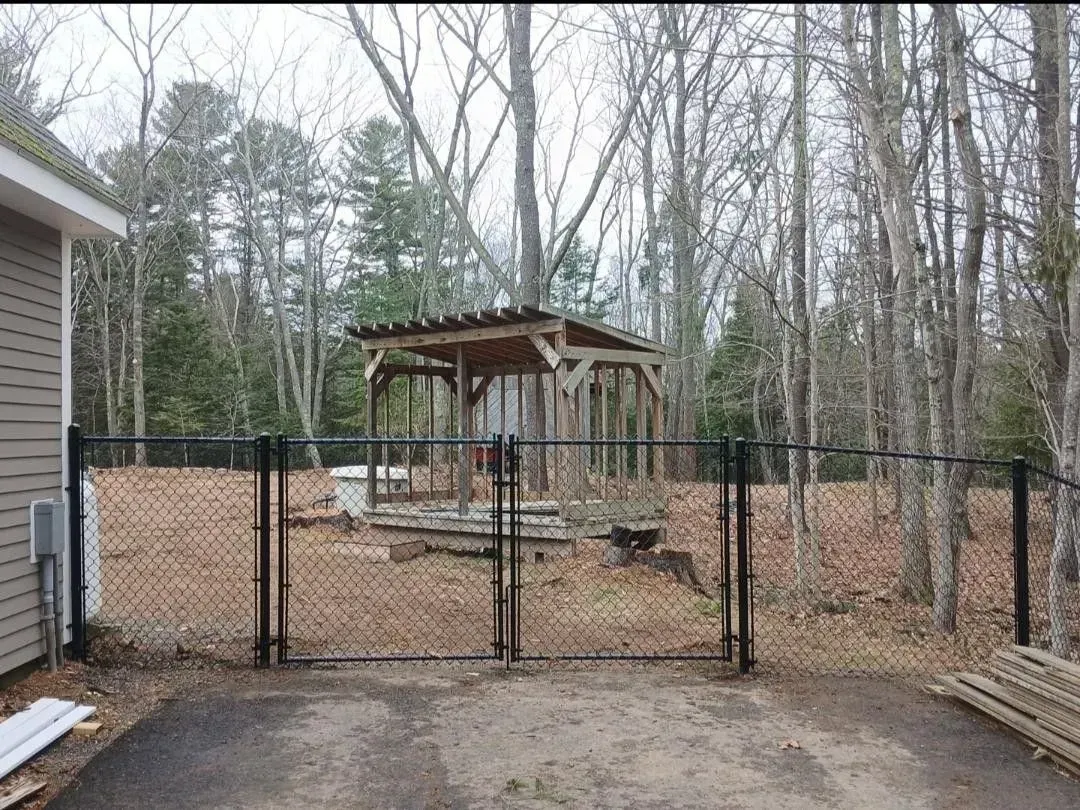 Backyard with chain-link fence and pavilion under construction among leafless trees