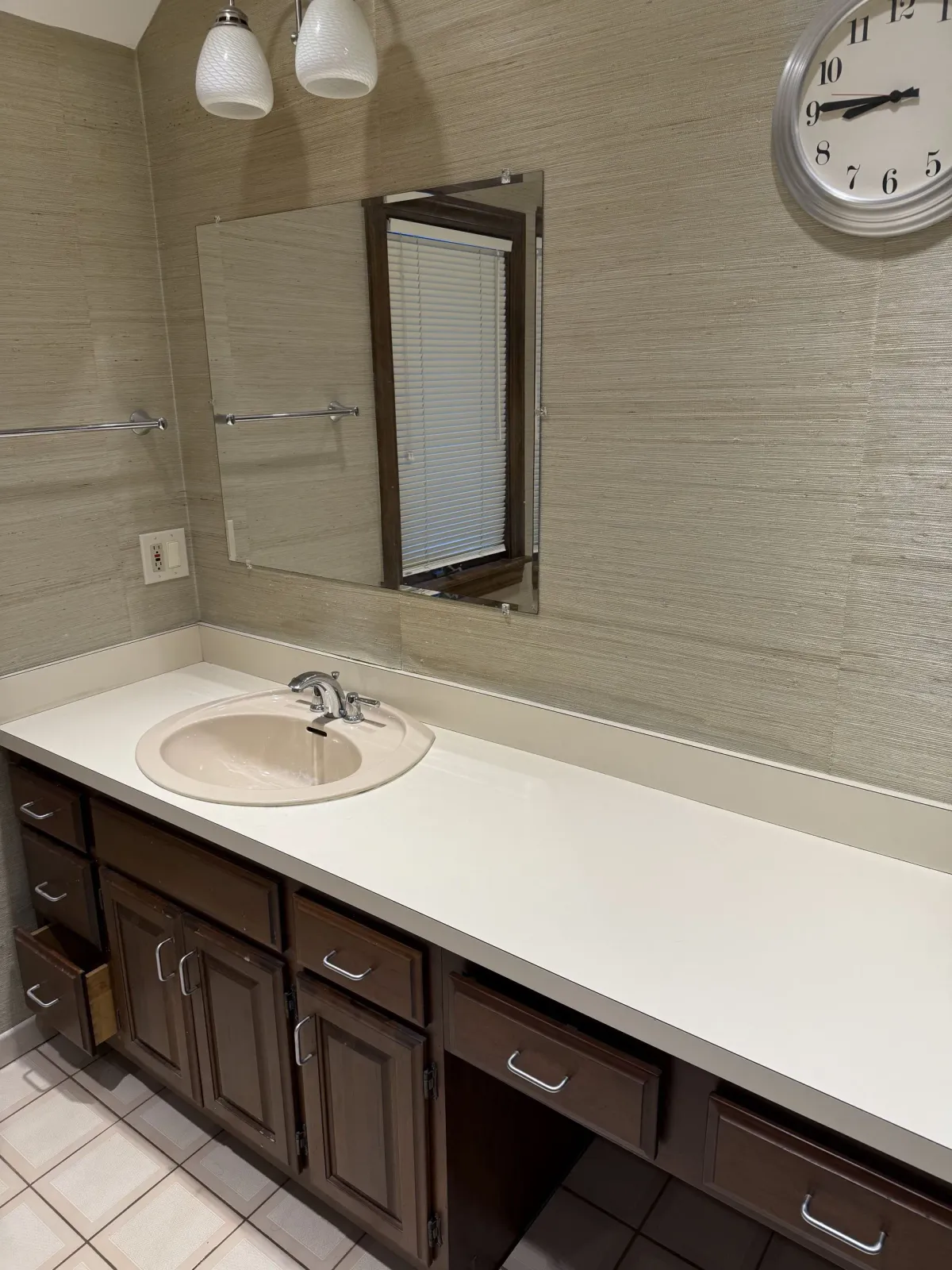 Bathroom with beige textured wall, dark brown cabinets, a white countertop, and a round sink.