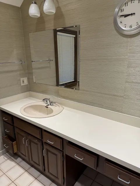 Bathroom with beige textured wall, dark brown cabinets, a white countertop, and a round sink.