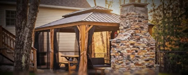 Cedar gazebo beside a tall natural stone fireplace chimney on a backyard patio in Concord, NH
