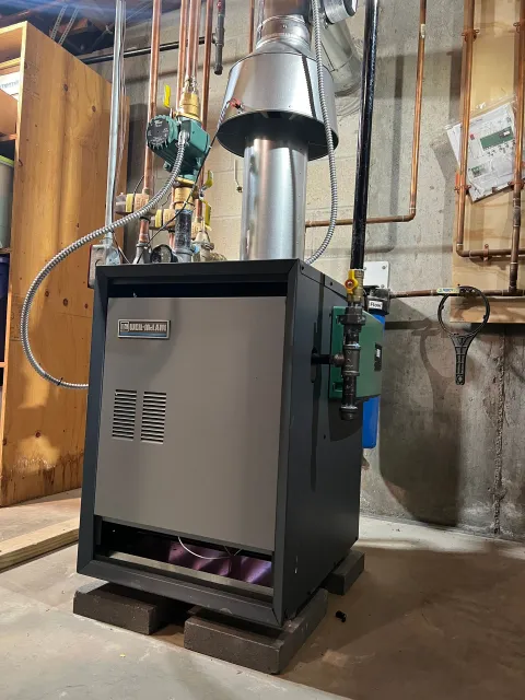 Gray industrial furnace with silver vent pipes in a basement utility room