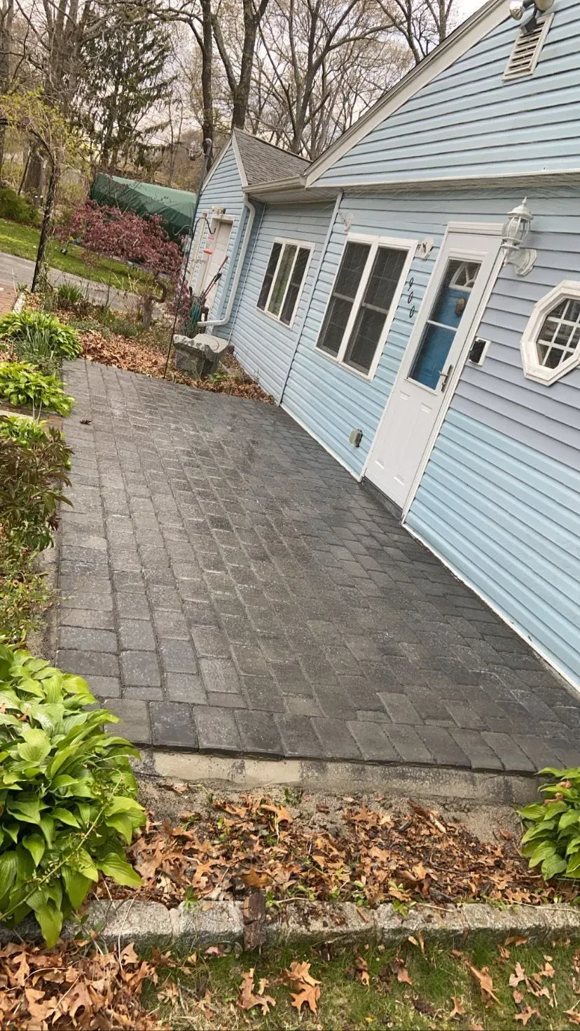 Brick patio next to a blue house with a white door and windows; fallen leaves on ground.